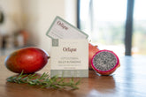 A package of Orlique liposomal glutathione supplement is displayed with a mango and a pomegranate in the background.